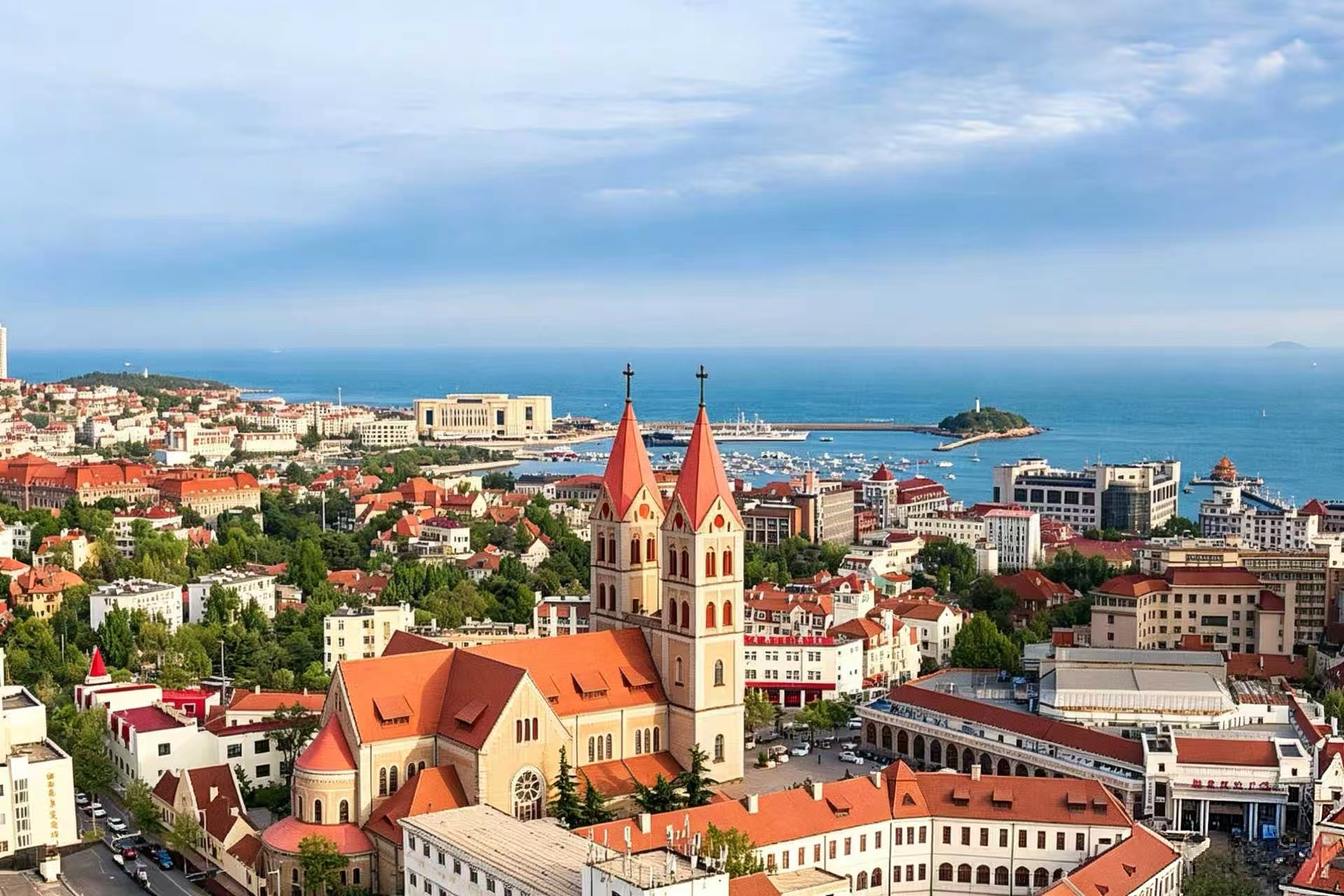 The red-tiled rooftops and green spires of Qingdao's old town, seen from a hillside overlooking the blue sea